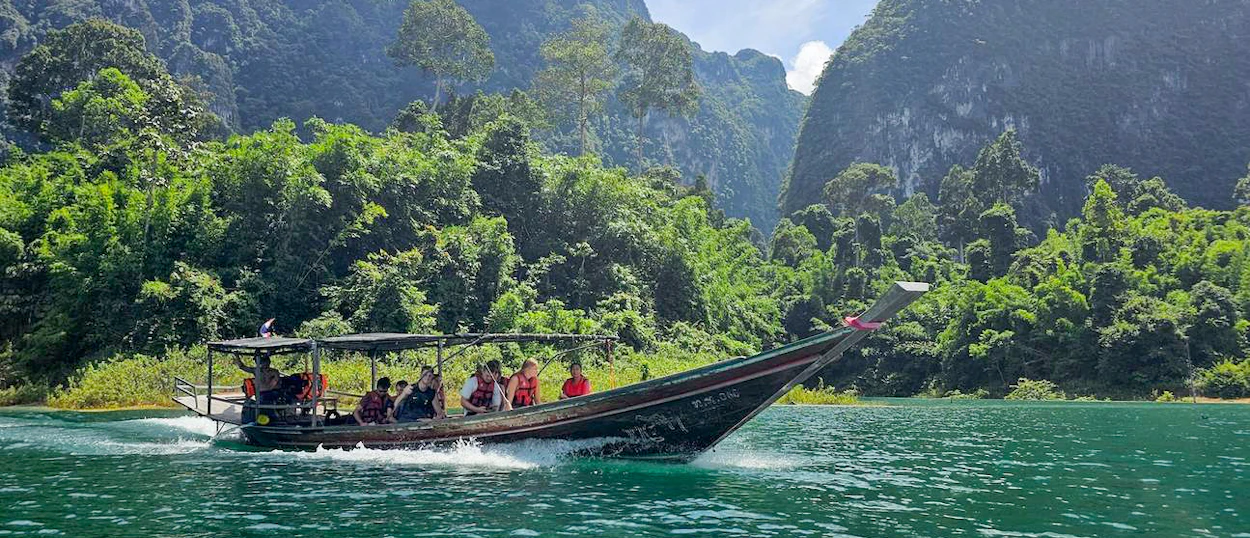 A longtail boat carries tourists across Chiewlan Lake surrounded by lush green mountains in Khao Sok.