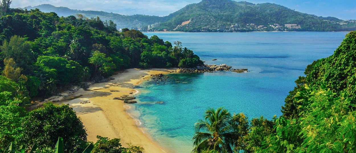 Stunning tropical beach in Phuket with turquoise water, golden sand, and lush green hills.