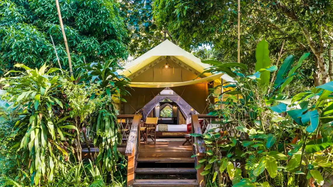 A safari tent on a wooden deck among lush jungle at Hintok River Camp in Kanchanaburi, Thailand.