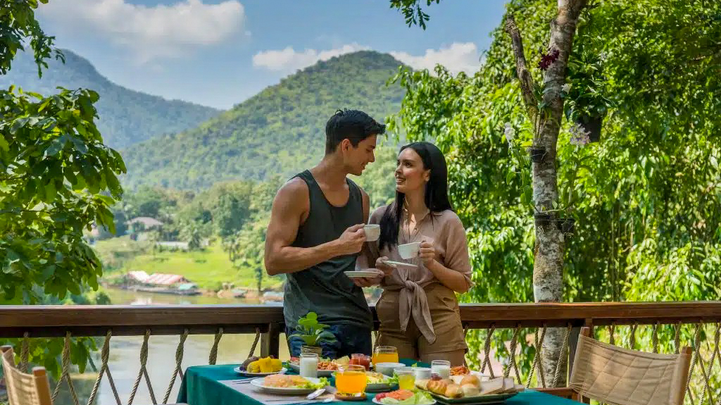 A couple share breakfast on a jungle terrace above the river valley at Hintok River Camp, Thailand.
