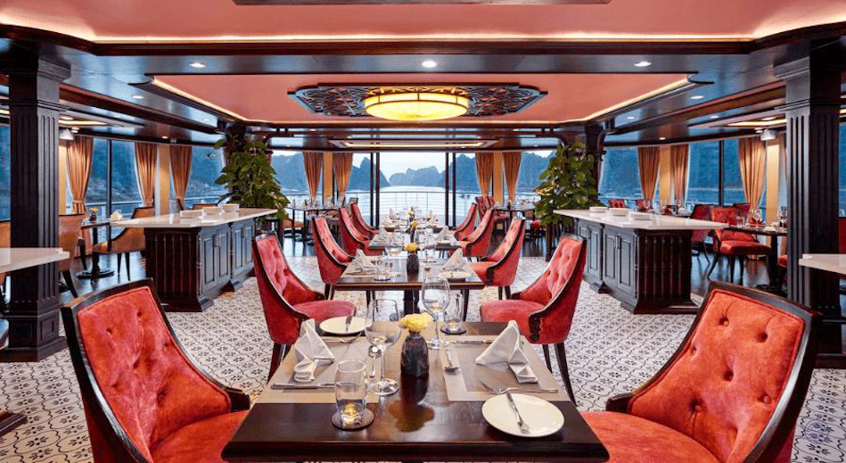 Elegant cruise ship dining room with red chairs, set tables, and a panoramic view of Ha Long Bay.