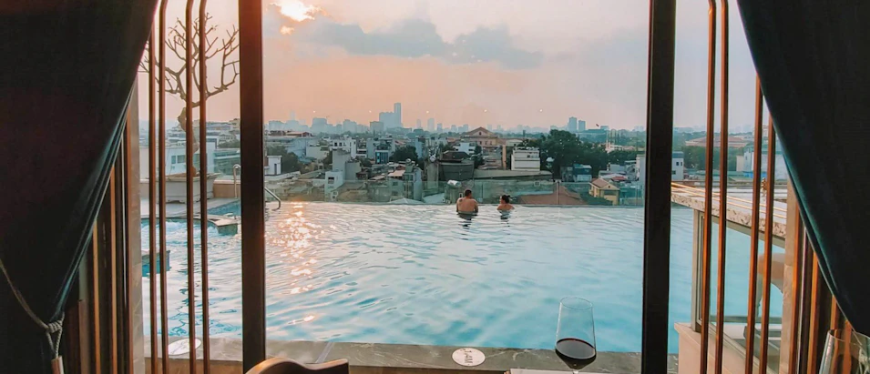 Couple relaxing in a rooftop infinity pool overlooking the Hanoi city skyline at sunset.