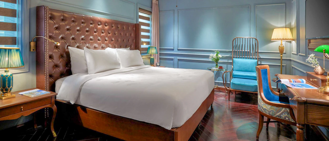 Elegant hotel room in Hanoi with a large bed, tufted headboard, and stylish blue decor.