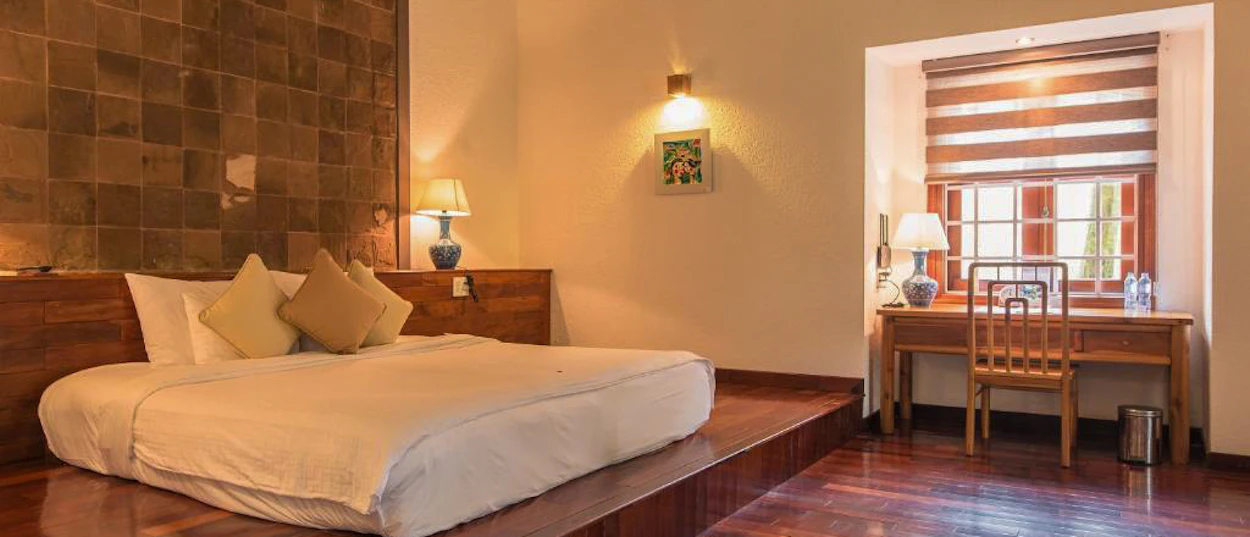 A spacious, warm-lit hotel room in Hue with a large bed and a wooden desk by a window.
