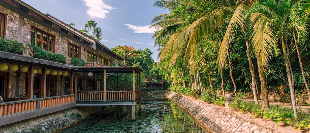 Serene traditional building with wooden balconies overlooking a canal lined with tropical palm trees in Hue.