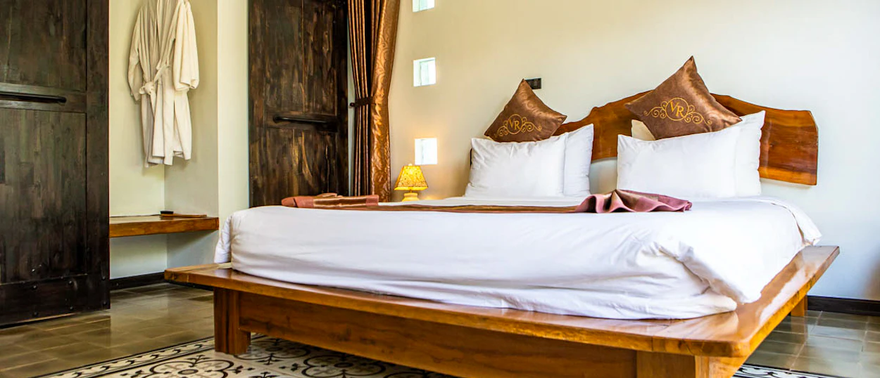 A serene bedroom at Victory Road Villas in Phong Nha, featuring a large wooden bed and white linens.