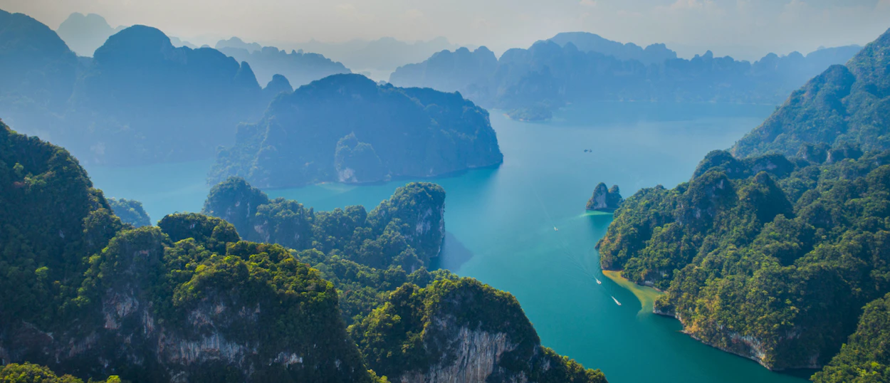 Boats navigate tranquil turquoise waters surrounded by majestic, tree-covered limestone karsts in Tam Coc, Vietnam.
