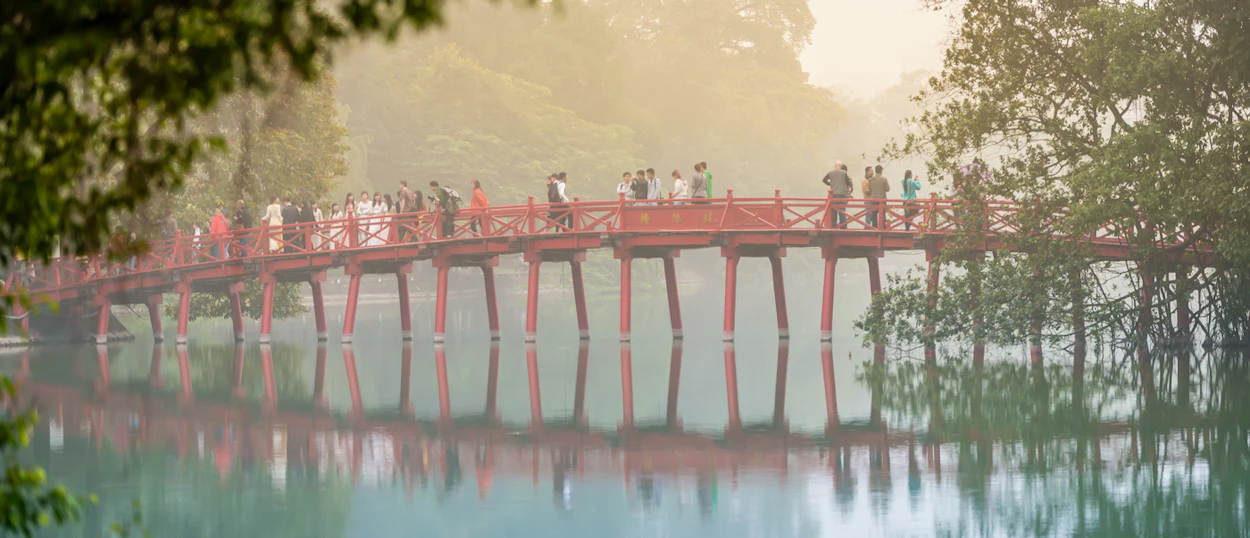People walk across the iconic red Huc Bridge over Hoan Kiem Lake in Hanoi, Vietnam.