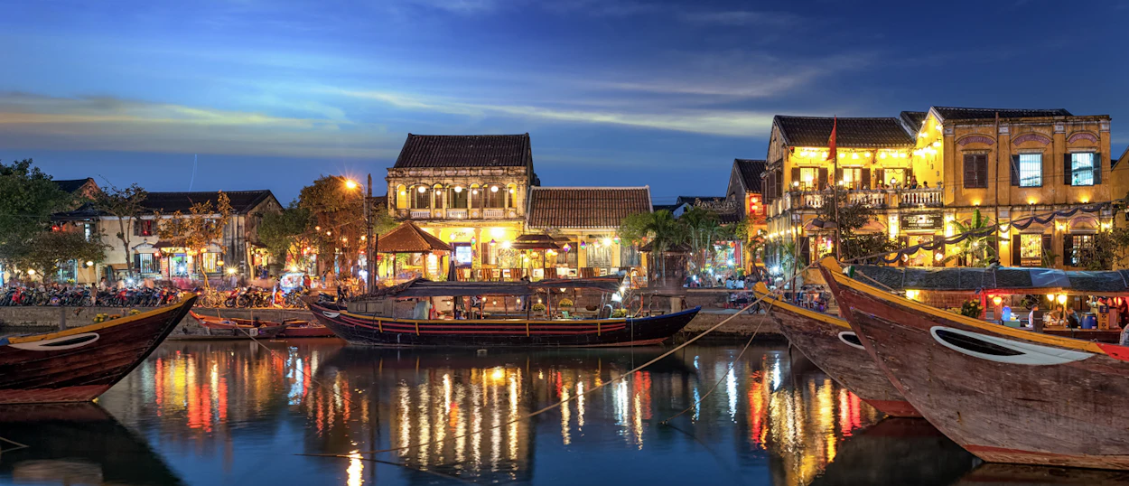 Hoi An's ancient town glows at night, with traditional boats on the river reflecting warm lights.