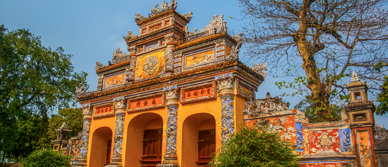 Ornate yellow imperial gate with multiple arches and intricate colorful details under a clear blue sky in Hue.